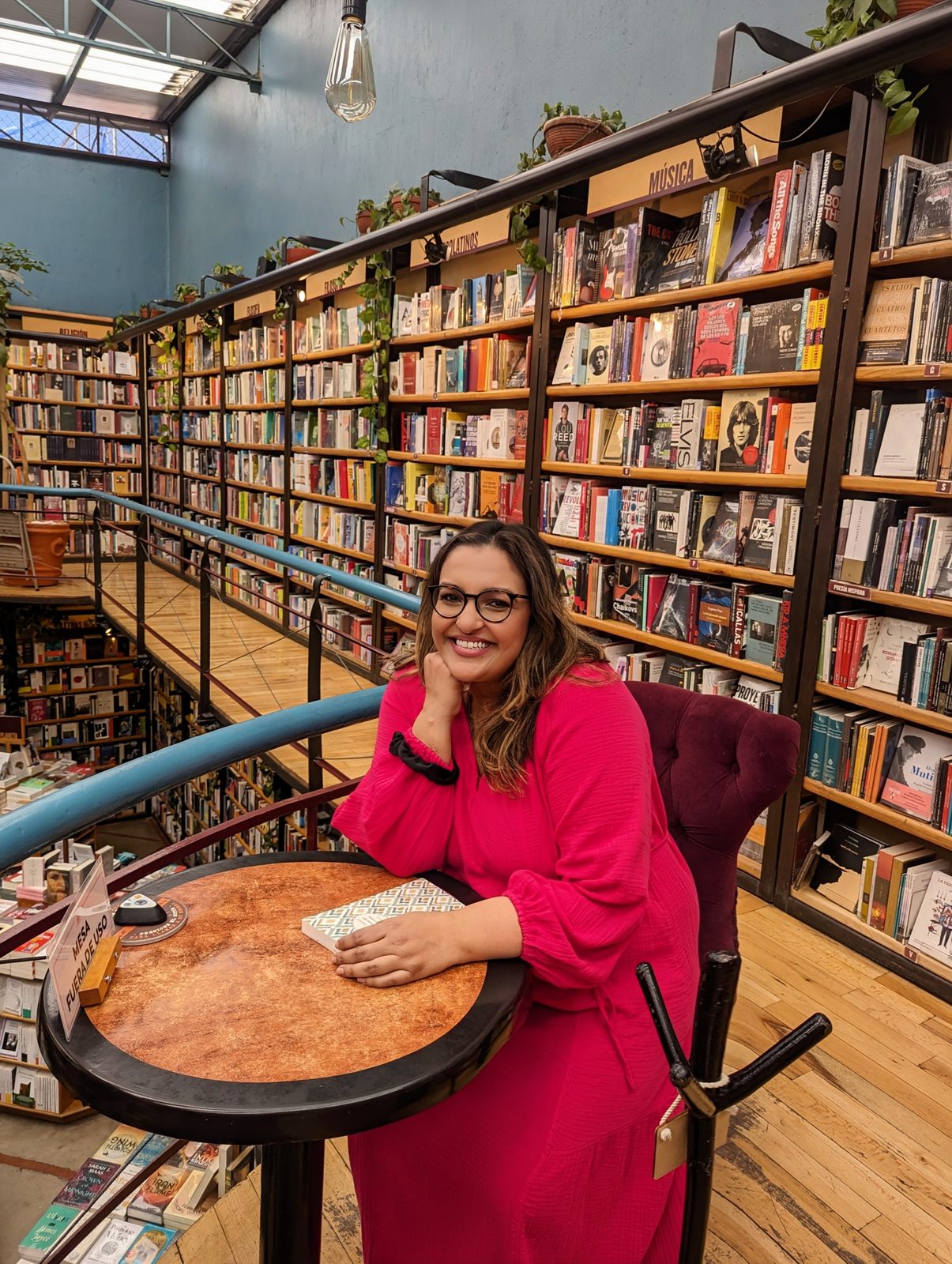 Ashmi smiling at a cafe table inside a bookstore, surrounded by shelves of books