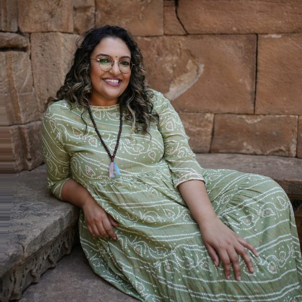 Ashmi relaxing against warm sandstone in a green block-print dress