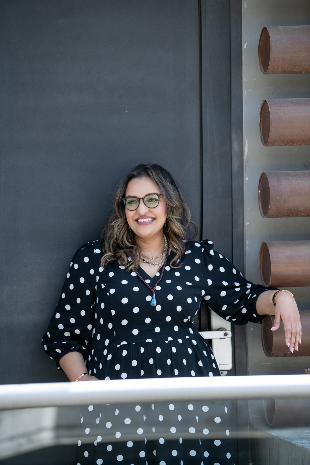 Ashmi in a polka dot dress, smiling confidently against a dark modern wall